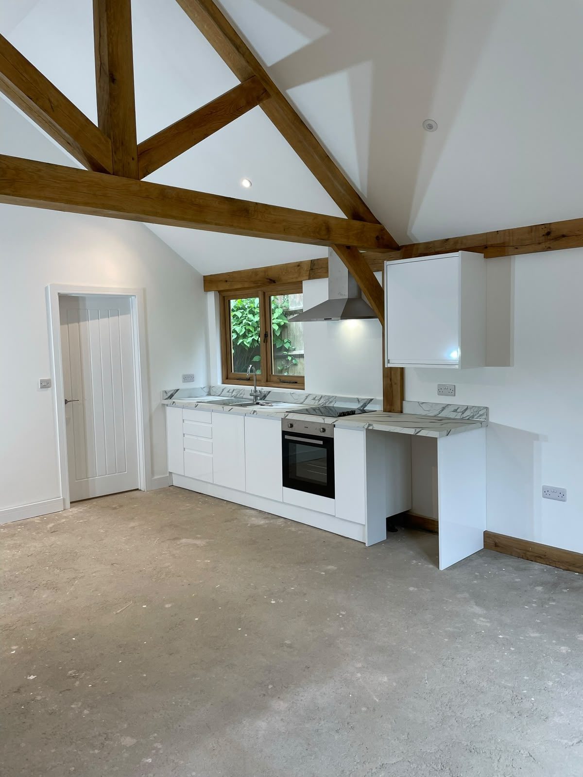 White kitchenette beneath the vaulted oak beams of an annex